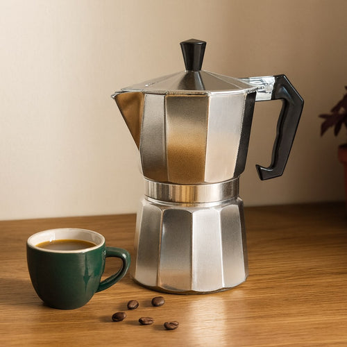 Cafetera moka clásica de aluminio en un rincón de cocina con taza de espresso